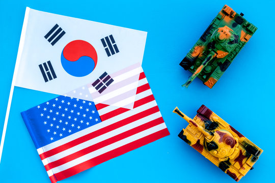 War, confrontation concept. Korea, USA. Tanks toy near korean and american flag on blue background top view