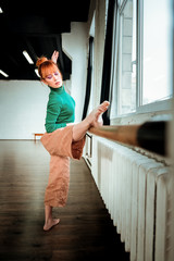Young professional ballet dancer with hair bun doing legs stretching