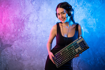 Professional Girl Gamer in MMORPG Strategy Video Game. She's She posing over colorful blue and pink background with a gaming keyboard. She Wears Gaming Headset.