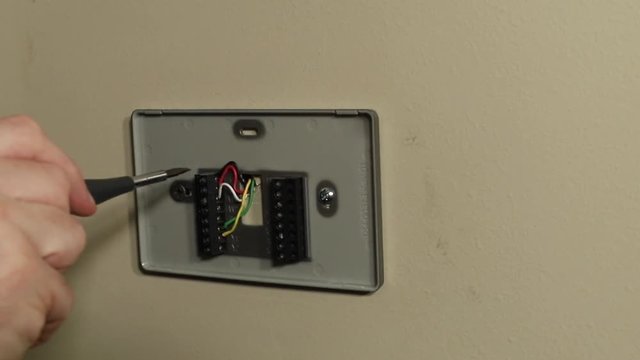 Hand using tools to wire thermostat wires