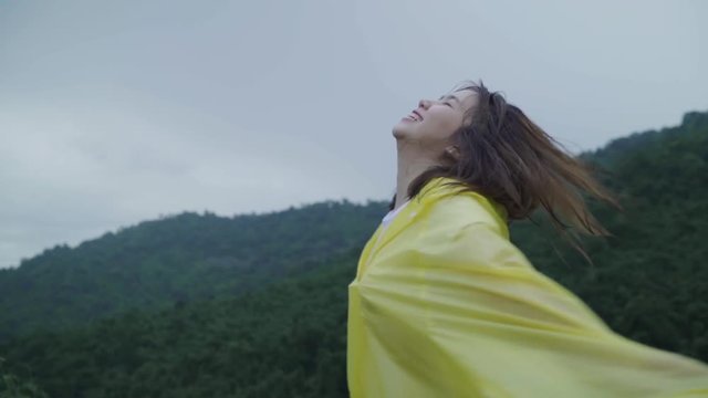 Slow motion - Young Asian woman feeling happy playing rain while wearing raincoat walking near forest. Lifestyle women enjoy and relax in rainy day.