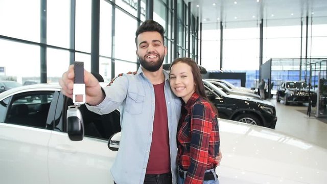 A young happy couple buys a new car. Smiles and shows the keys