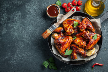 Baked chicken wings in barbecue sauce with sesame seeds and parsley in a cast iron pan on a dark concrete table. Top view with copy space © Vasiliy