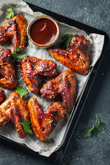 Roasted chicken wings in barbecue sauce with sesame seeds and parsley in a baking tray on a dark table. Top view. Tasty snack for beer on a dark background. Flat lay