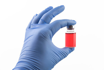 Doctor in gloves holding medicine bottle for injection. Medical glass vials and syringe for vaccination. Liquid red drug or vaccine for treatment, flu in laboratory, hospital, healthcare, or pharmacy 