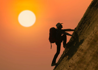 Silhouette of backpacker climbing on mountain at sunset or sunrise