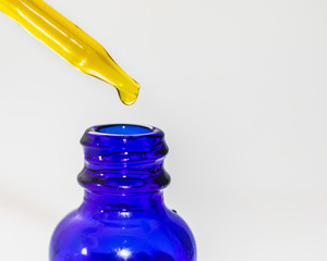 CBD oil tincture dropping into blue bottle up close isolated on white background