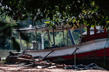 Fototapeta na wymiar Old wooden motor boat Parked on the land on the river side in Thailand,Vintage colors picture.