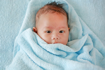 Portrait of cute infant baby boy in towel lying on bed after bath. 