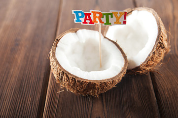 Coconut on the textural wooden background. Fragmented coconut close up. Topper inscription party 