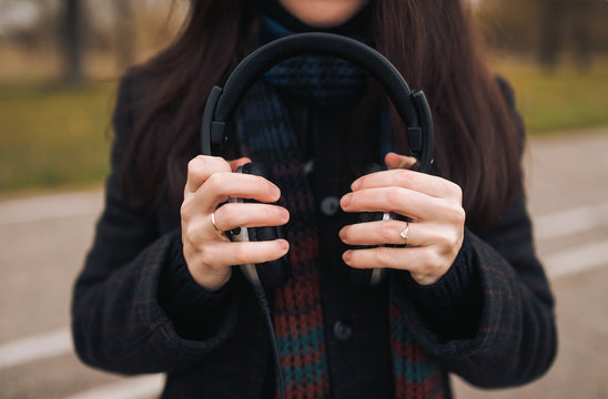 The girl is holding big headphones. Listen to music on a walk in the park.