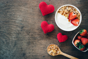 Top view of yogurt in a wooden bowl with granola,fresh strawberry and spoon on white wooden table. Health food concept.