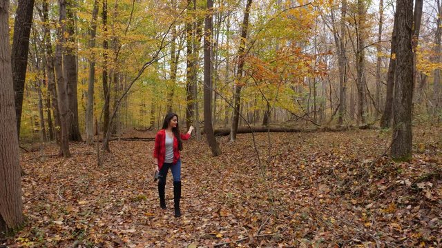 Woman holding a camera and looking for composition in autumn forest. Hiking in nature. 