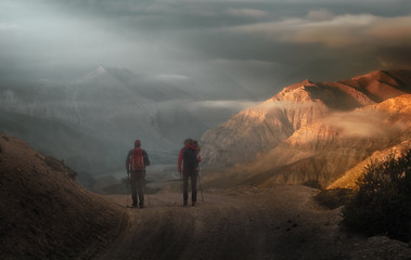 Two hikers with backpacks go high in the mountains of the Nepal.