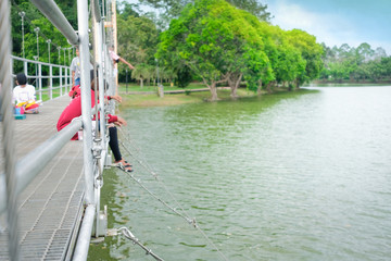 People enjoy feeding fish on suspension bridge. Selective focus