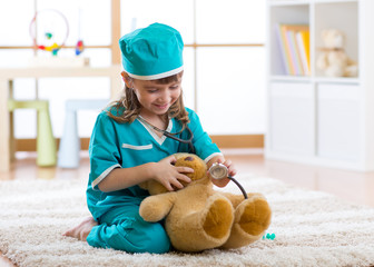 Kid weared doctor clothes playing with teddy bear in nursery