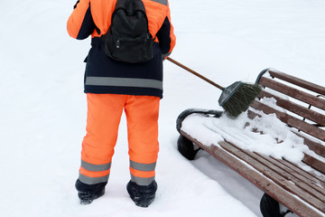 Snow removal, municipal worker with a broom clears snow in winter. Woman in uniform sweeps snow...