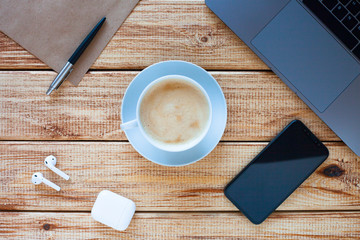 Top view of a laptop computer keyboard with phone, cup of coffee and headphones on the wooden background. Business, office and work concept. 