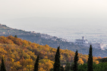 Beautiful view of Assisi town (Umbria) and St.Francis church in autumn from an unusual place, behind an hill with orange and yellow trees