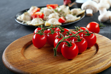 Close up view on fresh cherry tomatoes  for use as cooking ingredients for ravioli. Tomato on wooden desk in front of mushrooms and ravioli. Free copy space for text. Italian cuisine. Recipe picture