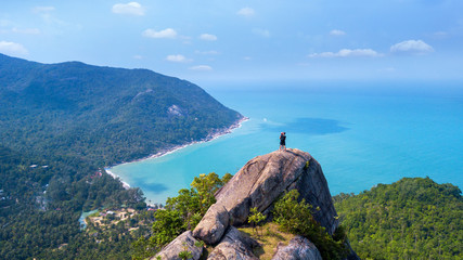 Man and woman standing on cliff's edge and looking into a sand beach of koh Phangan island,Thailand