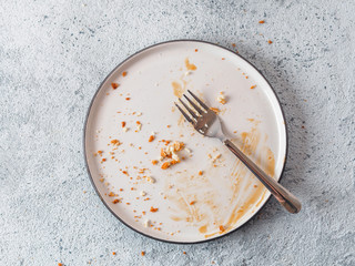 Empty dirty dish after cheesecake with caramel sauce and dessert fork. White rustic trendy modern...