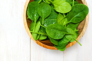 Fresh green spinach leaves on wooden bowl on white wooden rustic background top view copy space....