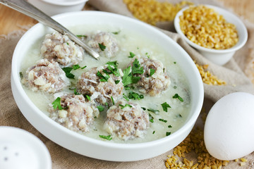 Armenian white sour soup on chicken broth with meatballs, bulgur and green parsley