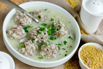 Armenian white sour soup on chicken broth with meatballs, bulgur and green parsley