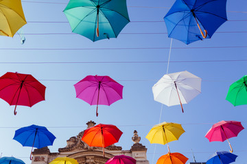 Fototapeta na wymiar Lviv city colorful umbrellas on the street. Colored umbrellas hanging in the sky. Palace of arts. Street decorations. Multicolored umbrellas over blue sky. 