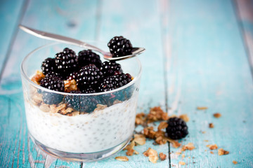 Chia pudding with granola and fresh blackberry in glass on blue wooden background, healthy food idea