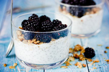 Chia pudding with granola and fresh blackberry in glass on blue wooden background, healthy food idea
