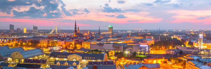 Fototapeta premium Beautiful aerial panorama of Riga center and Vansu, railroad bridges over Daugava river during amazing sunset. View of illuminated Riga city, capital of Latvia.