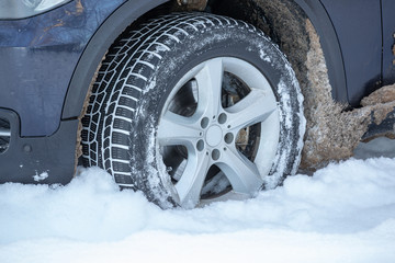 The wheel of a blue car stuck in the snow. The concept of a snowy winter, drifts on the road,...