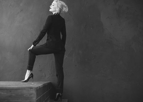 High Fashion Shot Of Sexy Blond Woman In Black Suit On Red Background, Portrait Of Elegantly Dressed Gorgeous Business Woman With Red Lips 