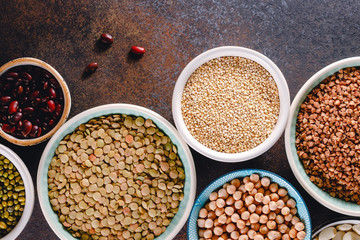 Top view on bowls with various grains on a textured dark background.