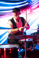 Fototapeta na wymiar Emotional drummer playing on drum set on stage in the color light 