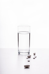 A glass of water on a white background and pills (drugs)