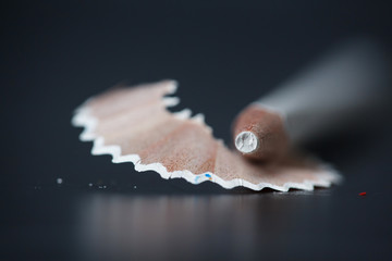 White pencil and shavings on black background. Closeup