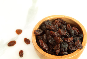 Dried raisins in wooden bowl on white marble background with copy space.