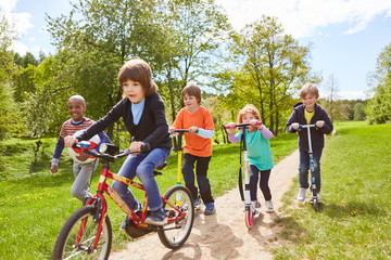 Kinder machen Wettrennen mit Roller und Fahrrad