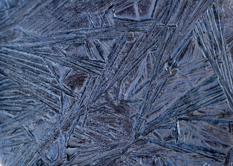 Window iced up in cold weather leaving a beautiful blue pattern on glass with selective focus.