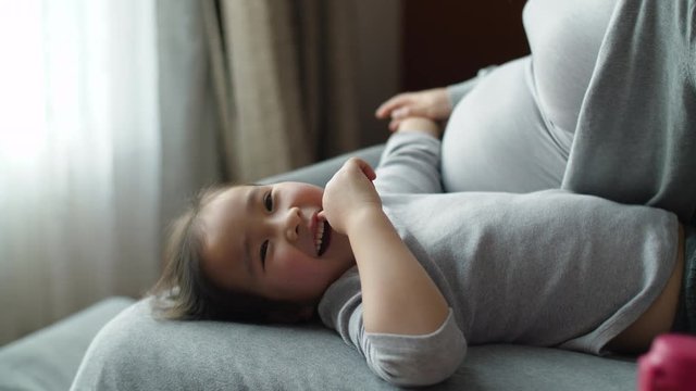 Lovely little Asian child having fun with her pregnant mother belly and touch expecting, curious about the coming baby in the family. pregnant woman with kid at home 4k footage, China two-child policy
