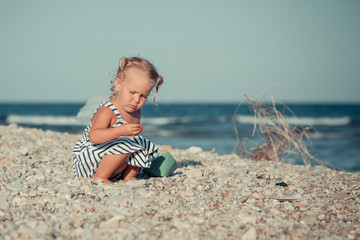 Pretty little girl playing with a paper boat by the sea