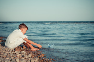 boy plays with a paper boat by the sea and dreams