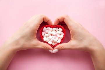 Female hands and red heart shape with marshmallows on pink background. Valentine's Day. Love. Holiday.