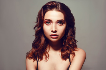 Beautiful caucasian woman with short brown curly hair. Portrait of a pretty young adult girl. Sexy face of an attractive lady posing at studio over grey background. Woman with pink natural make up.
