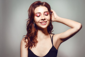Obraz premium Beautiful caucasian woman with short brown curly hair. Portrait of a pretty young adult girl. Sexy face of an attractive lady posing at studio over grey background. Pink natural make up girl smile.