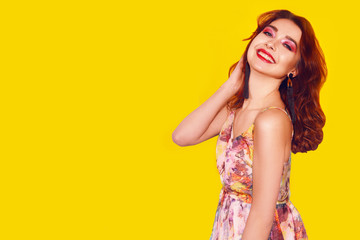 Fashion girl in dress on yellow background dancing. Pretty girl with long cerly flying hair and pink make up. Girl with long green earrings. Portrait with smile. Blithesome ginger lady having fun.