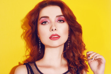 Fototapeta premium Fashion girl portrait on yellow background posing. Pretty brunette girl with long cerly hair and pink make up. Girl with long earrings. Portrait fashion model . Woman with pink make up. Beauty concept